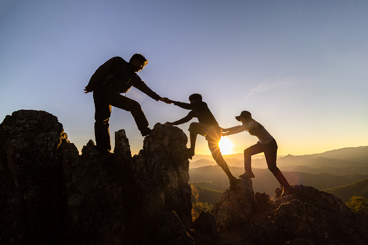 Silhouette of Teamwork of three hiker helping each other on top - Crédit: Tinnakorn/AdobeStock