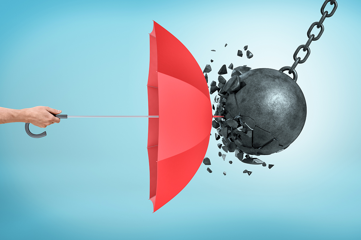 A male hand holding an open red umbrella which protects from a collision with a broken wrecking ball - Crédit: gearstd/AdobeStock