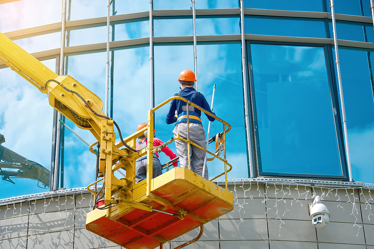 Window washing on high-rise office building in crane bucket - Crédit: Tricky Shark/AdobeStock