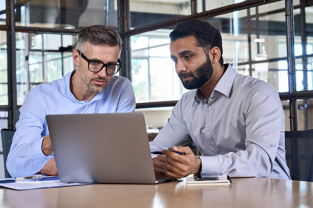 Two business men analysts discussing data management using laptop computer - Crédit: insta photos/AdobeStock