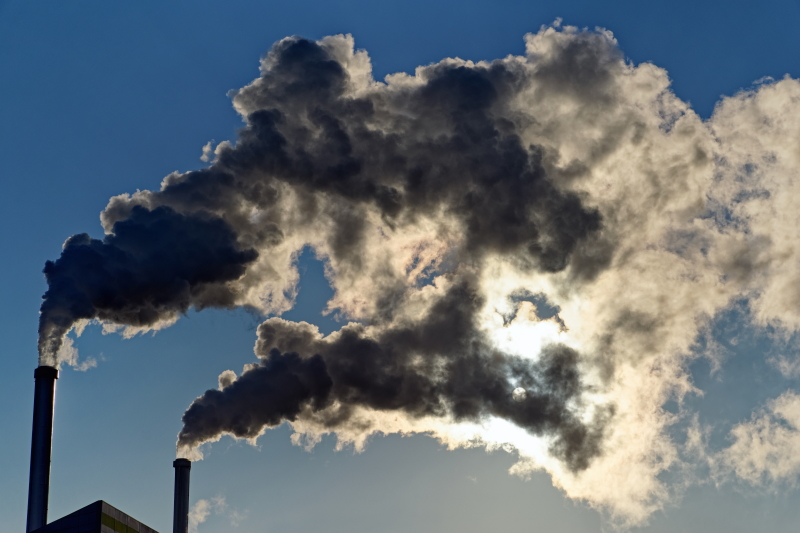 Photo de deux cheminés industrielles recrachant des fumées dans le ciel.