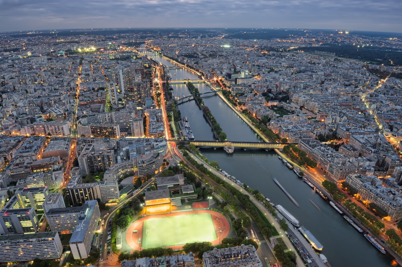 Vue aérienne et en début de soirée de Paris, avec la Seine entourée de bâtiments éclairés sur les deux rives.
