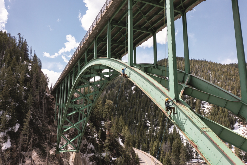 Deux nouvelles gammes de harnais de sécurité pour Petzl. (Hugo pédel – Red Cliff Bridge Colorado ┬® 2024 – Petzl Distribution – Vuedici.org) Des cordistes équipés de harnais de sécurité effectuent une missions en suspension sous un pont de grande hauteur aux États-Unis.