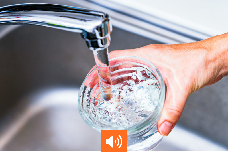 Main tenant un verre sous un robinet d'eau. © show999/AdobeStock